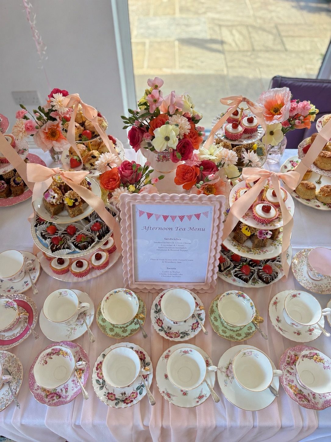 Tea party table with tiered dessert stands, floral arrangements, and vintage teacups.