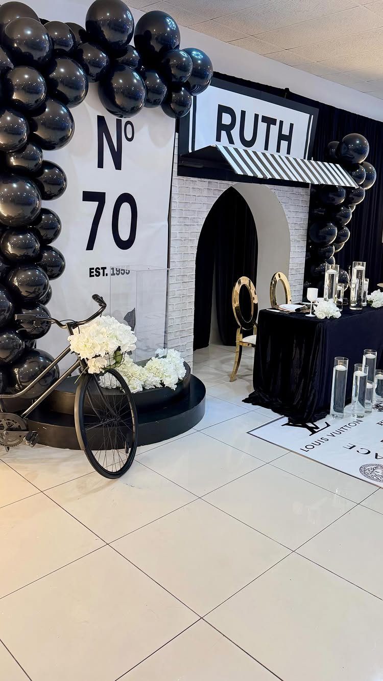 70th birthday party decoration with black balloons, white backdrop, and vintage bicycle.