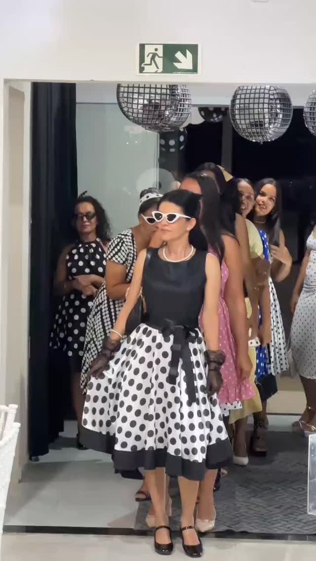 Women in 1950s polka dot dresses and cat-eye sunglasses at a themed party.