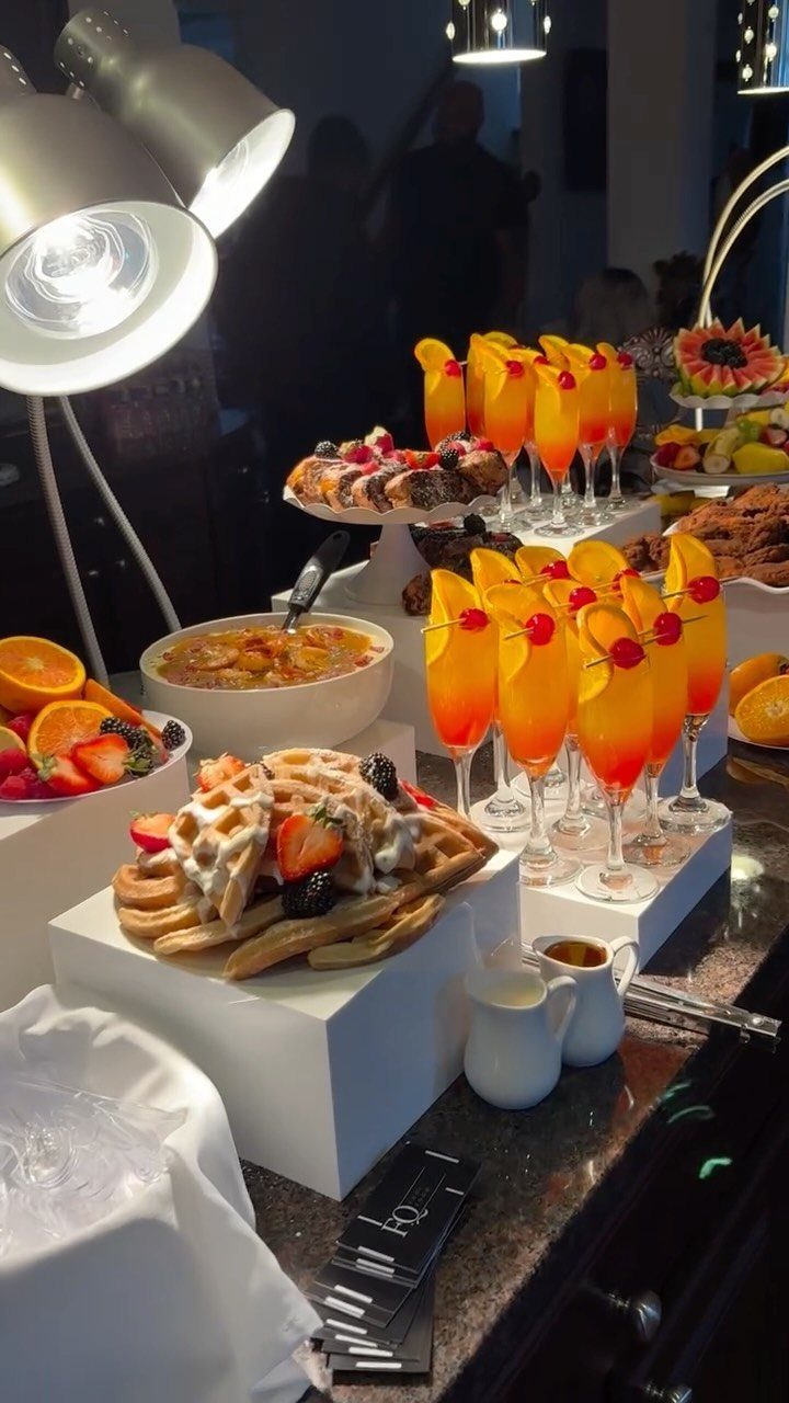 Breakfast buffet spread with waffles, fruit, and orange cocktails on a dark counter