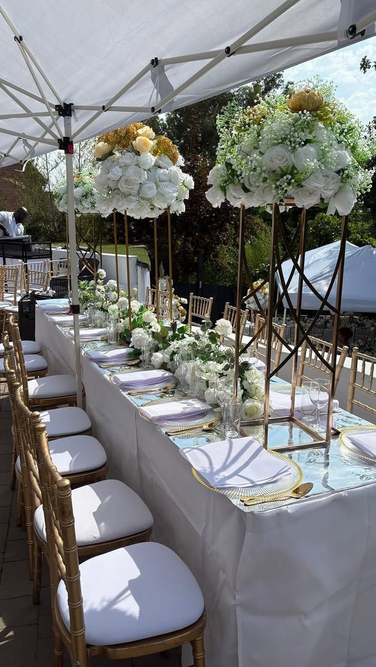 Elegant outdoor party table with white flowers, gold chairs, and white tent canopy
