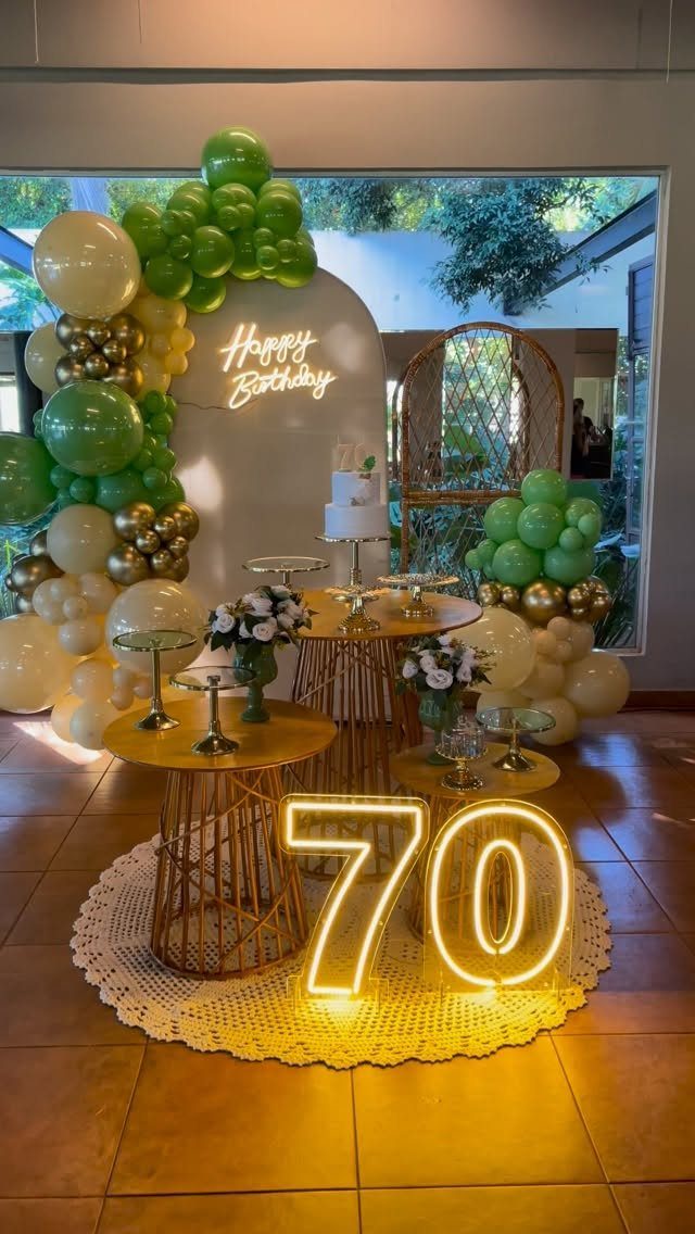 Birthday party decoration with green and gold balloons and a neon 70 sign.