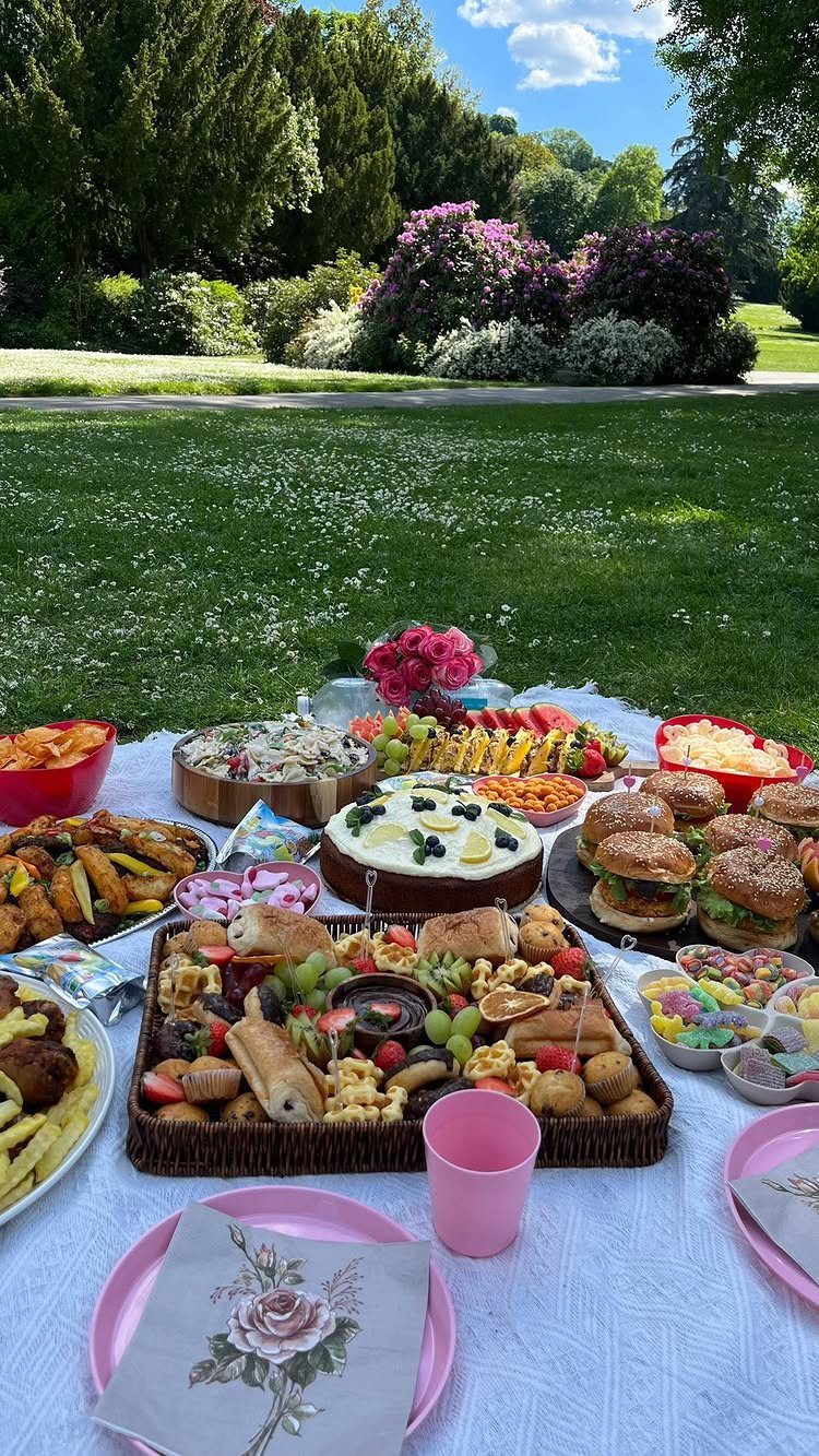 Assorted party foods on a white picnic blanket in a lush green garden.