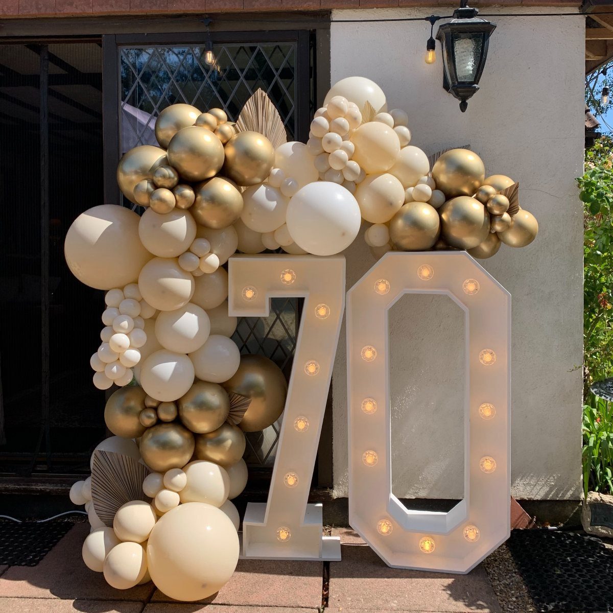 Large illuminated number 70 marquee surrounded by gold and white balloons outdoors
