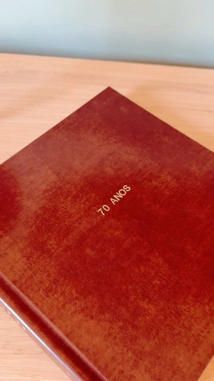 Reddish-brown leather book with gold embossed text reading 70 ANOS on wooden table