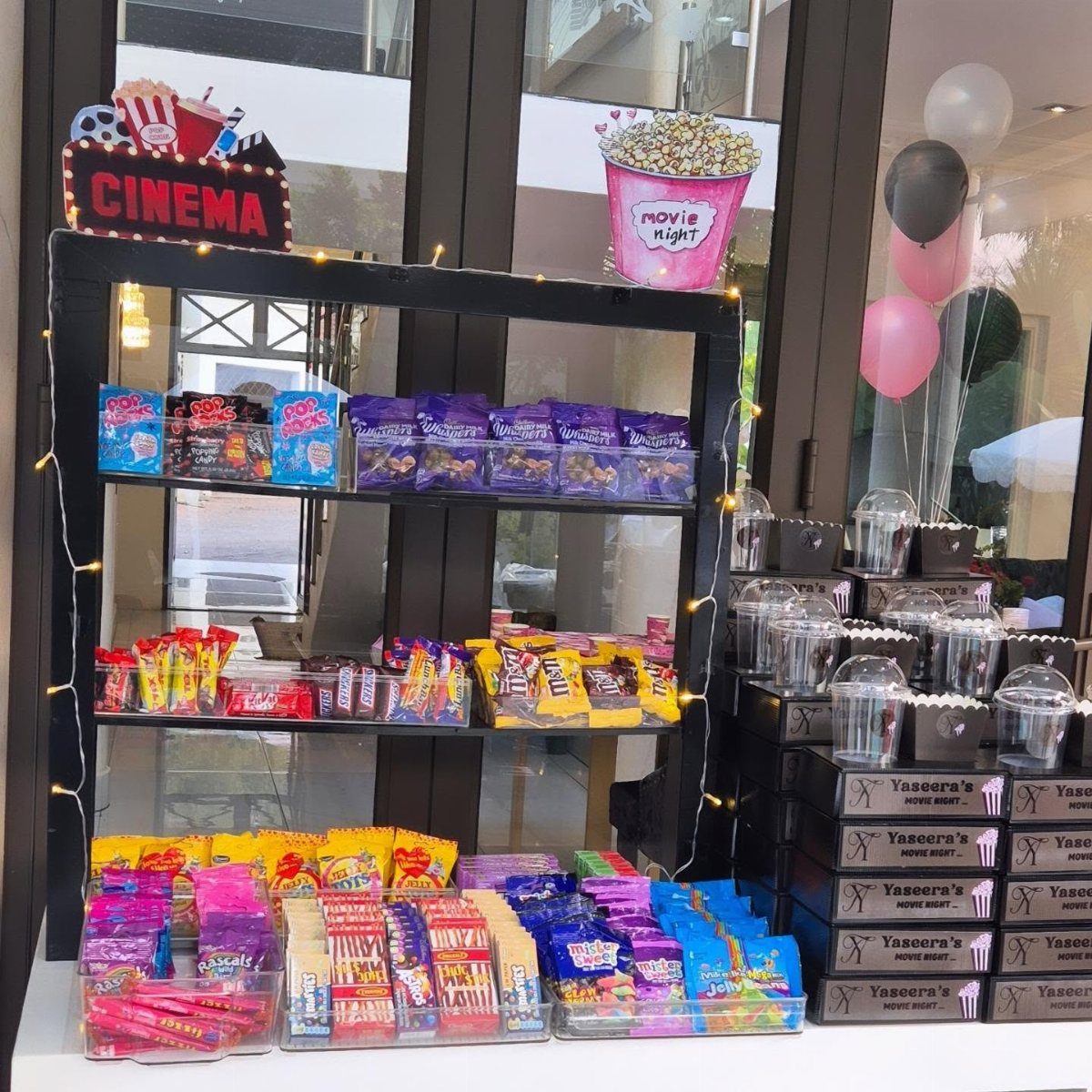 Cinema-themed snack station with candy, popcorn, and balloons for a birthday party.