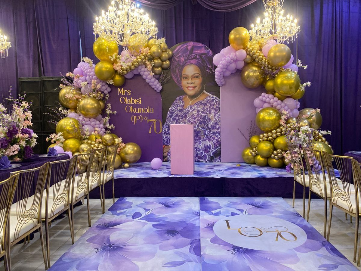 Purple and gold birthday party decorations with a large portrait and balloon arches.