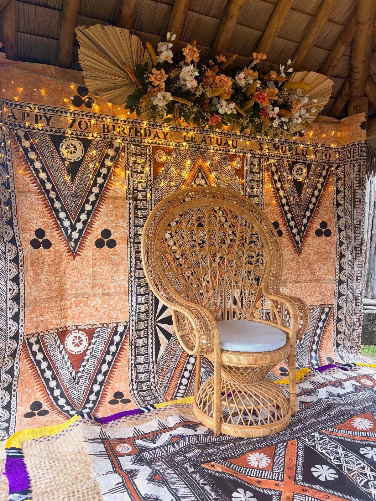Wicker peacock chair in front of a 70th birthday backdrop with floral decorations