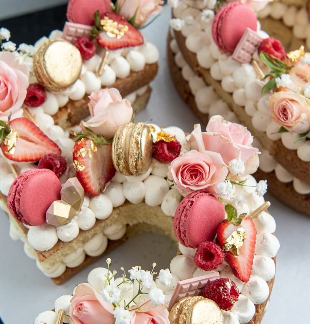 Number-shaped cream cake decorated with pink roses, macarons, and fresh strawberries.