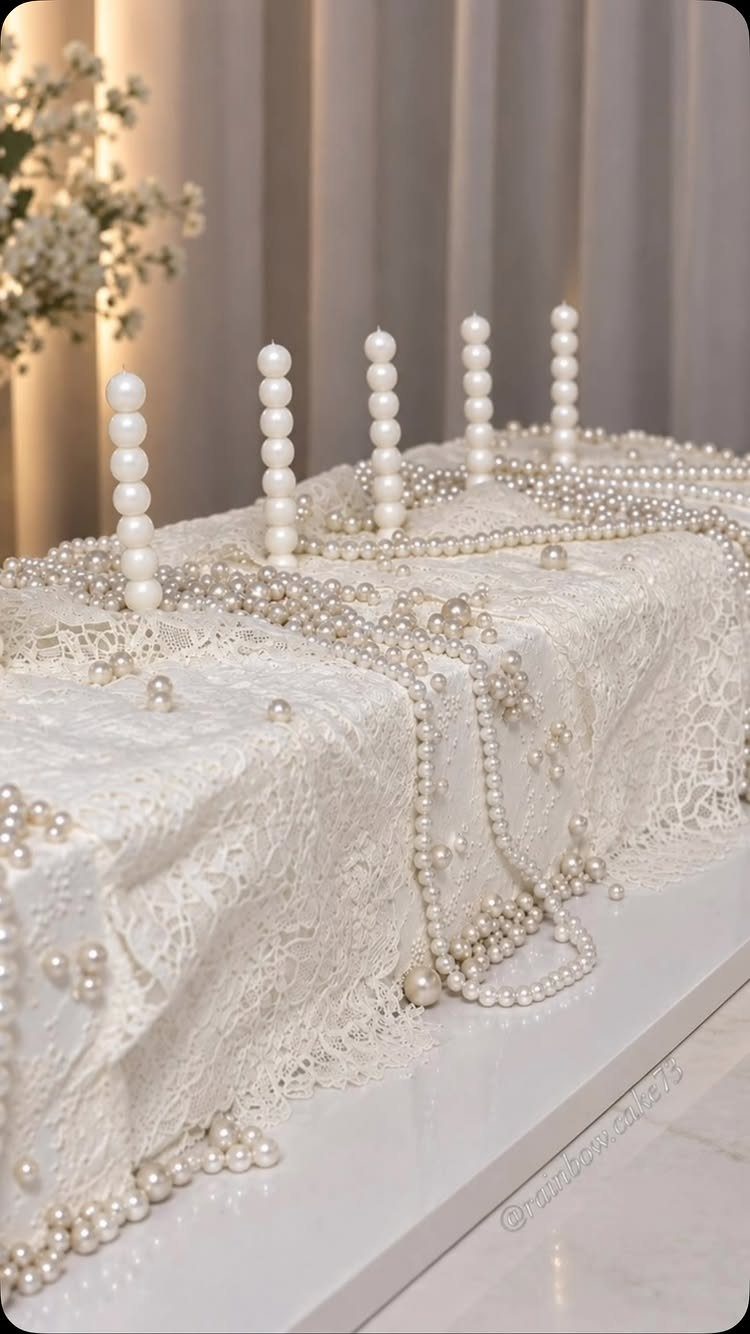White lace cake decorated with edible pearls and pearl-textured candles on top.