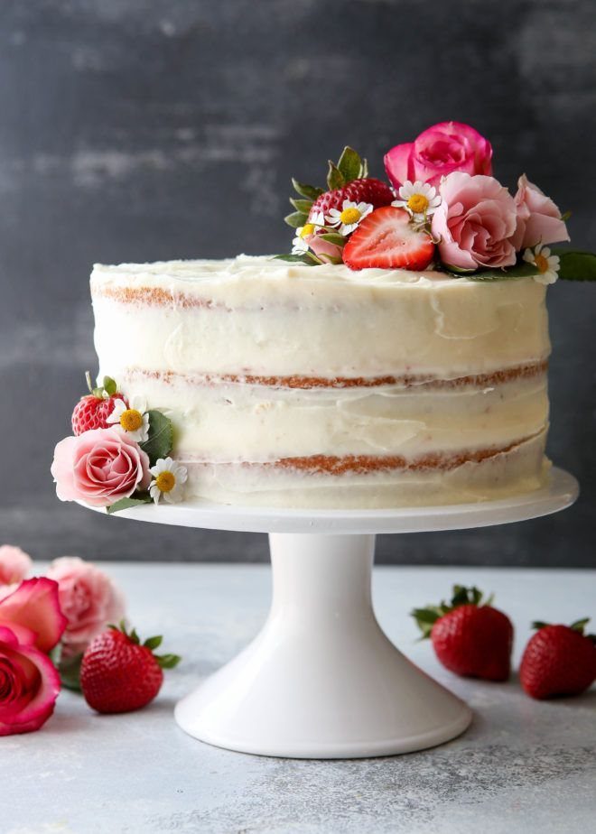 Semi-naked white frosted cake decorated with pink roses and fresh strawberries on stand