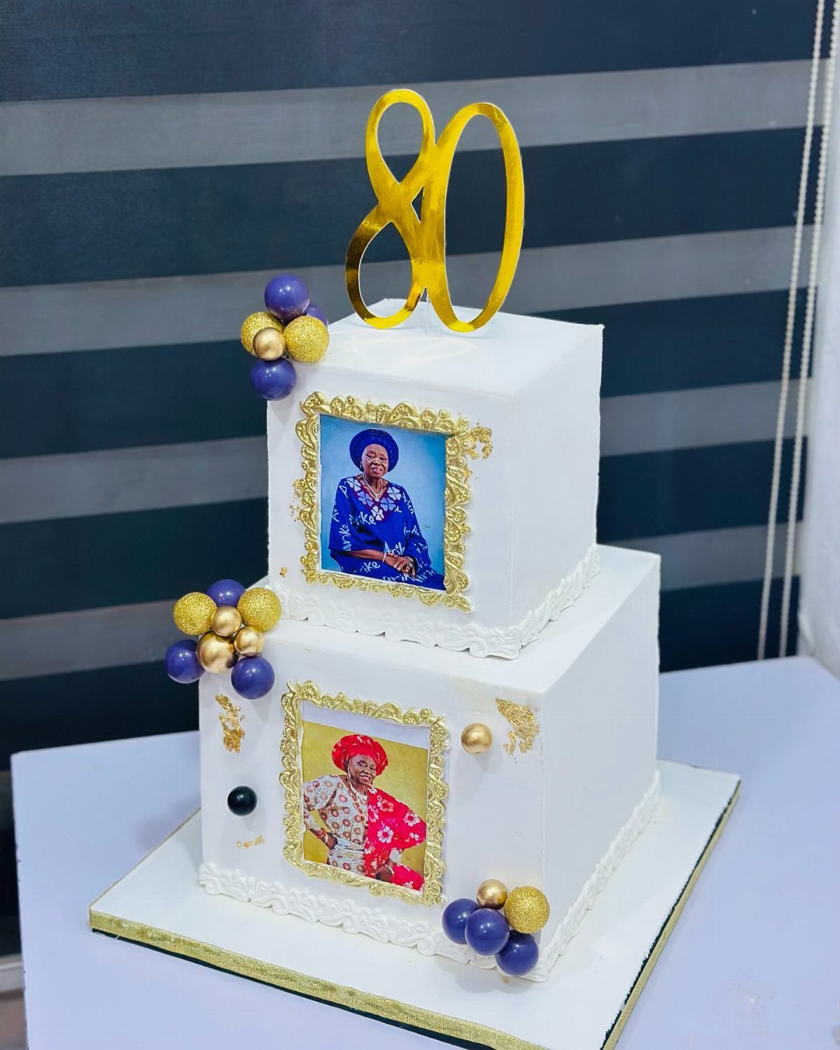 Two-tier white square cake with edible photos of a woman and gold 80 topper