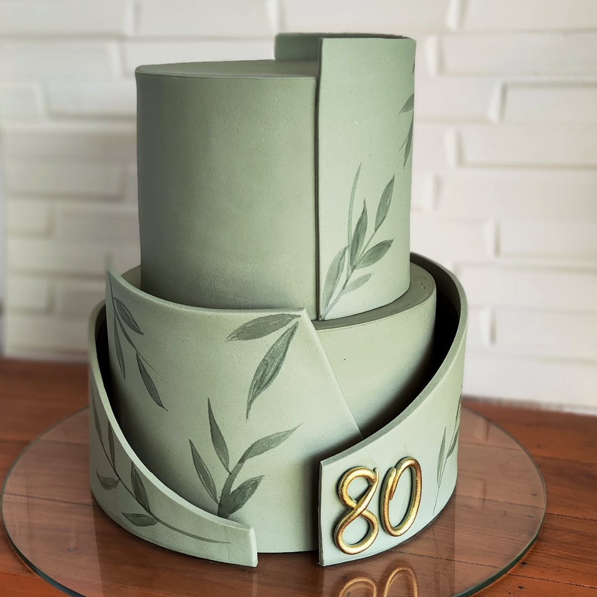 Sage green two-tier birthday cake with painted leaves and a gold number 80.