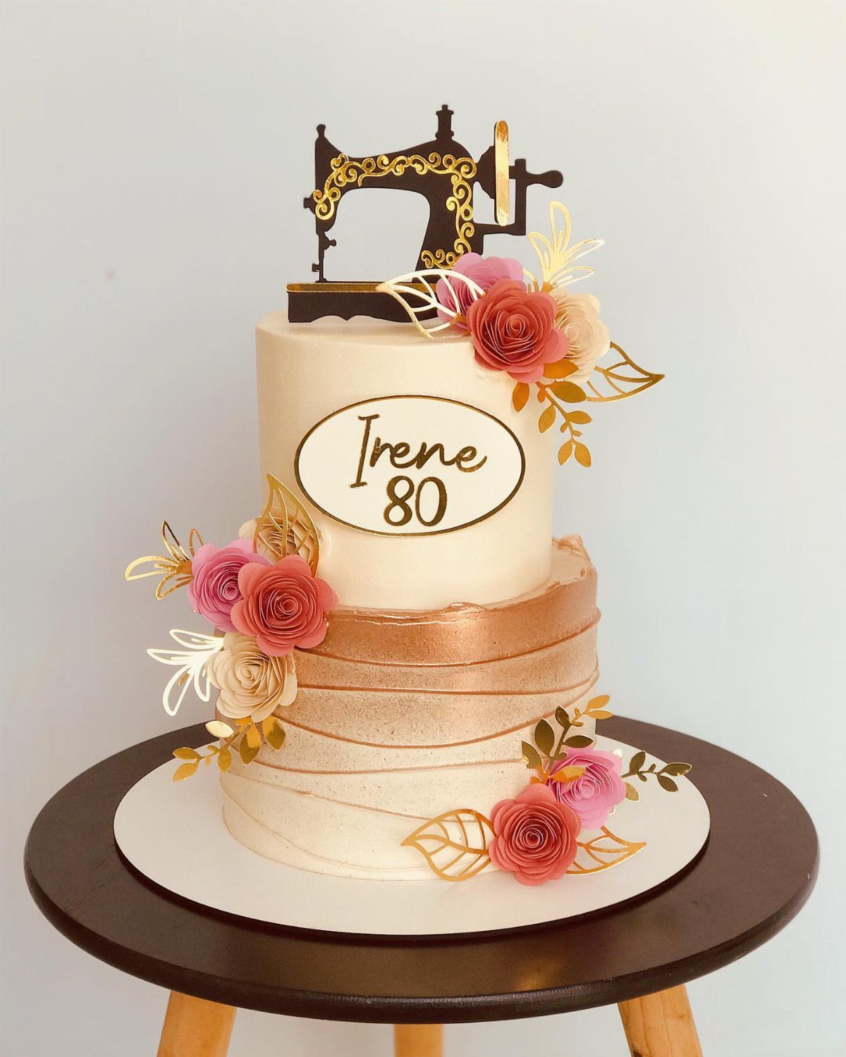 Two-tier white birthday cake with pink roses and a sewing machine topper for Irene 80