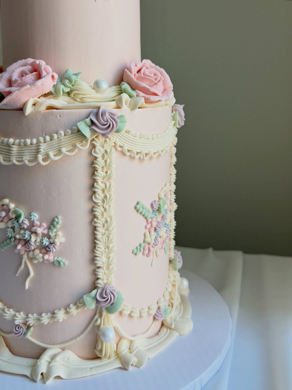 Two-tier light pink cake with cream frosting swags and pink and purple roses.