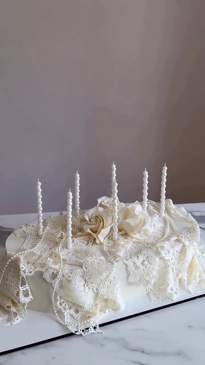 White frosted cake draped in cream lace with roses and tall white candles.