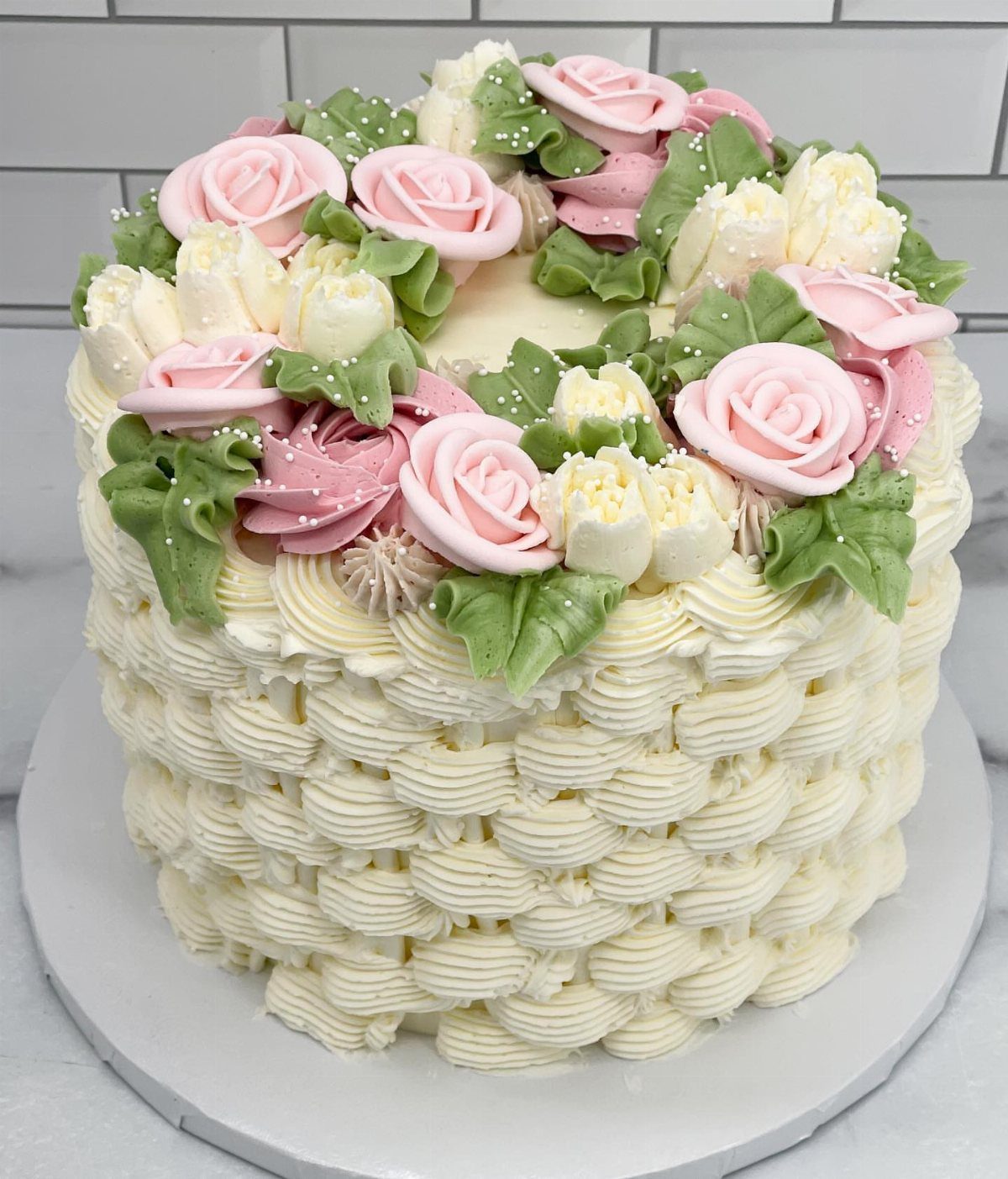 White buttercream cake with basketweave texture topped with pink and white frosting roses.