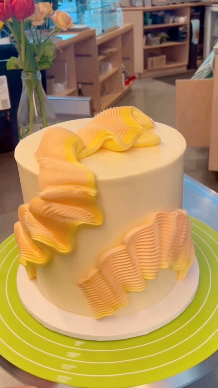 Pale yellow cake with decorative orange and yellow buttercream ruffles on a turntable.