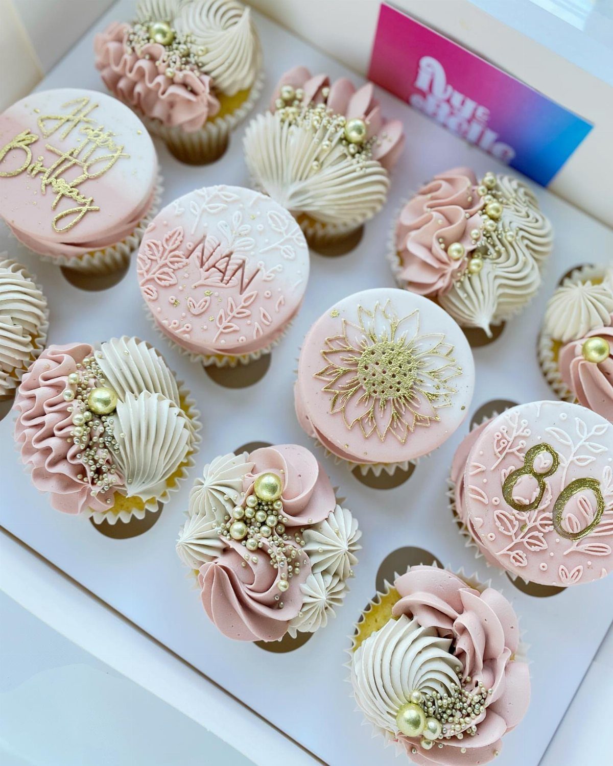 Decorated birthday cupcakes with pink and white frosting, gold pearls, and number 80.