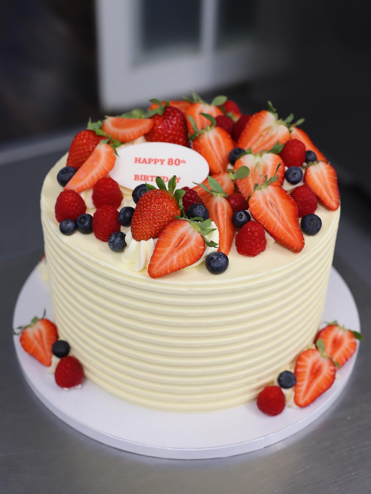 White frosted birthday cake topped with fresh berries and a Happy 80th Birthday plaque