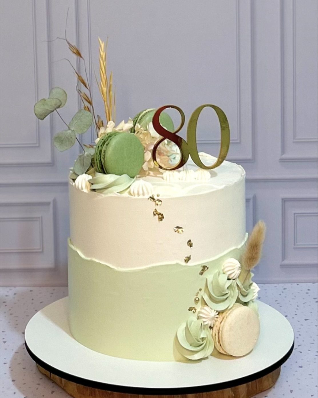 Two-tier white and pale green cake with macarons and gold 80 topper.