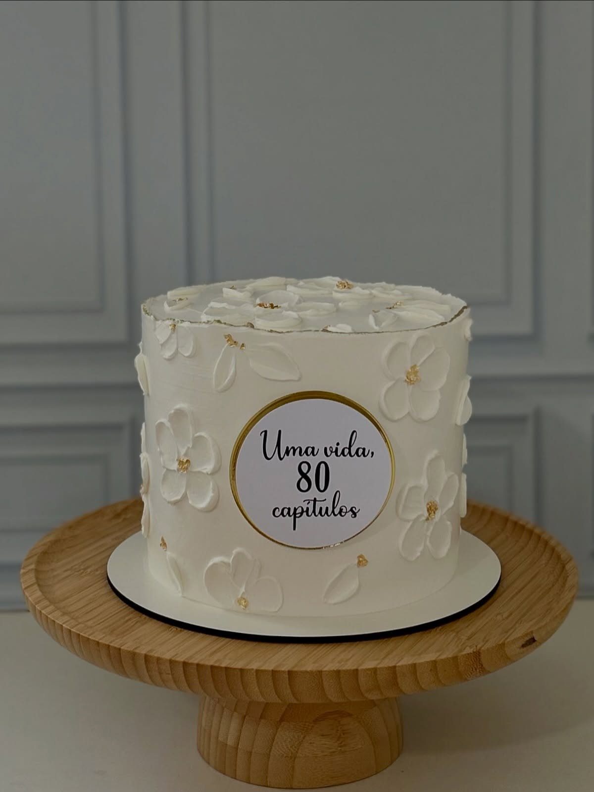 White buttercream cake with floral decorations and a plaque celebrating an 80th birthday.