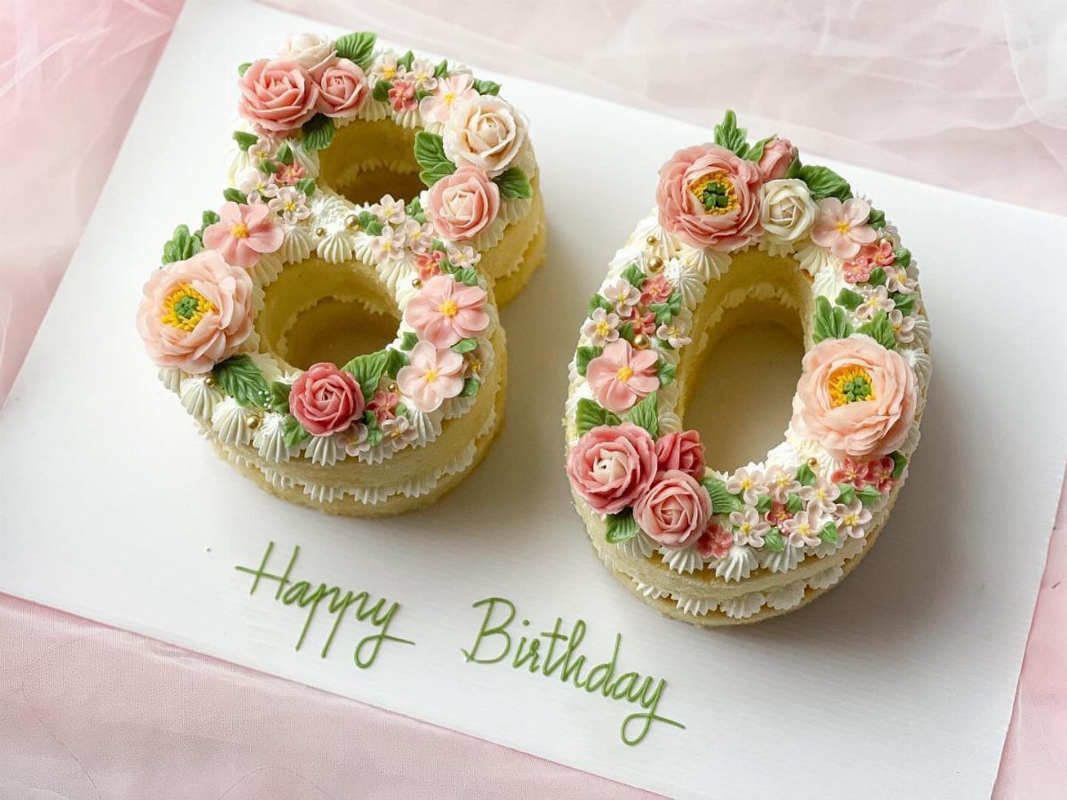 Number 80 birthday cake decorated with pink and peach buttercream flowers on white frosting
