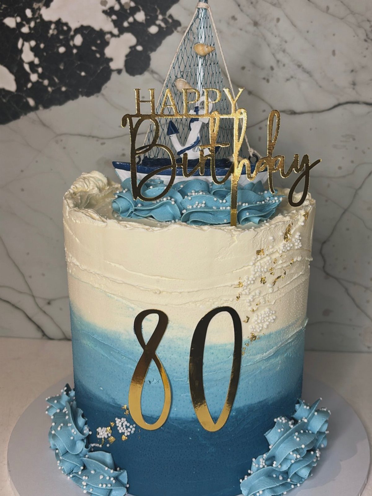 Blue and white ombre birthday cake with gold 80 topper and sailboat decoration