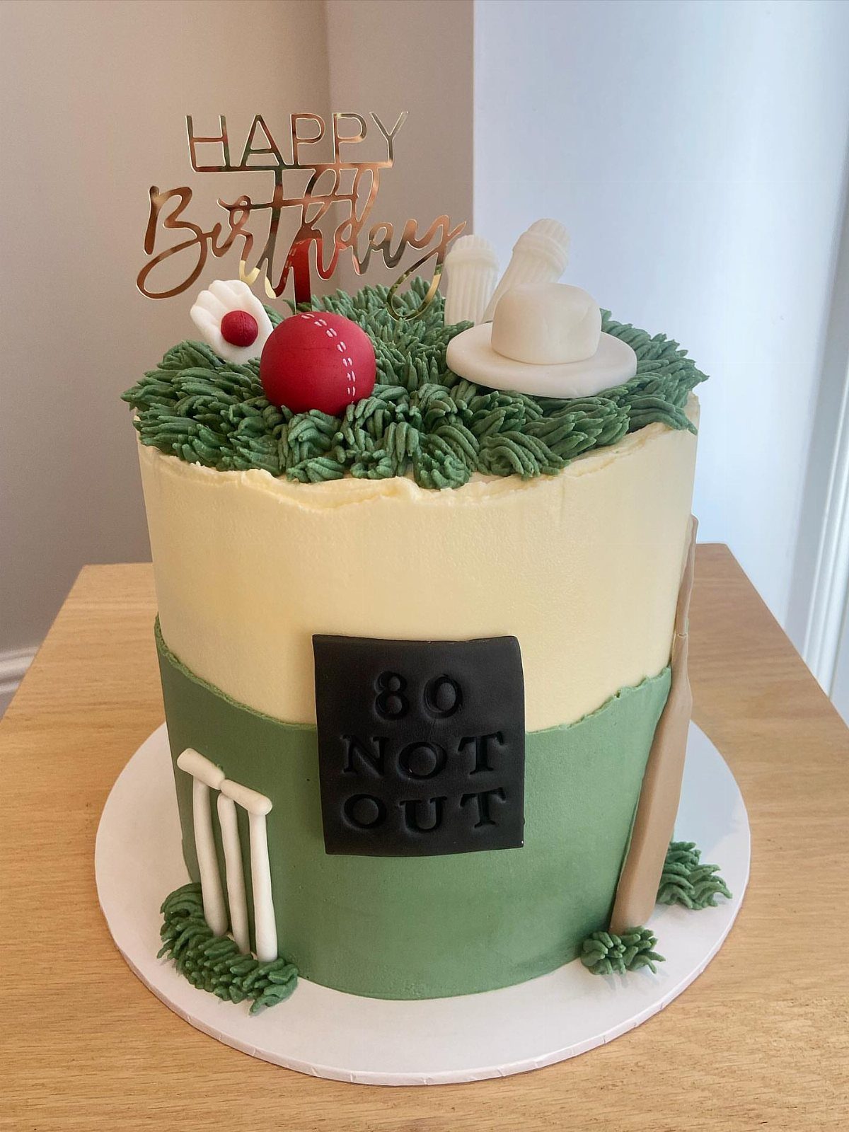 Cricket themed birthday cake with red ball, bat, and 80 Not Out plaque.