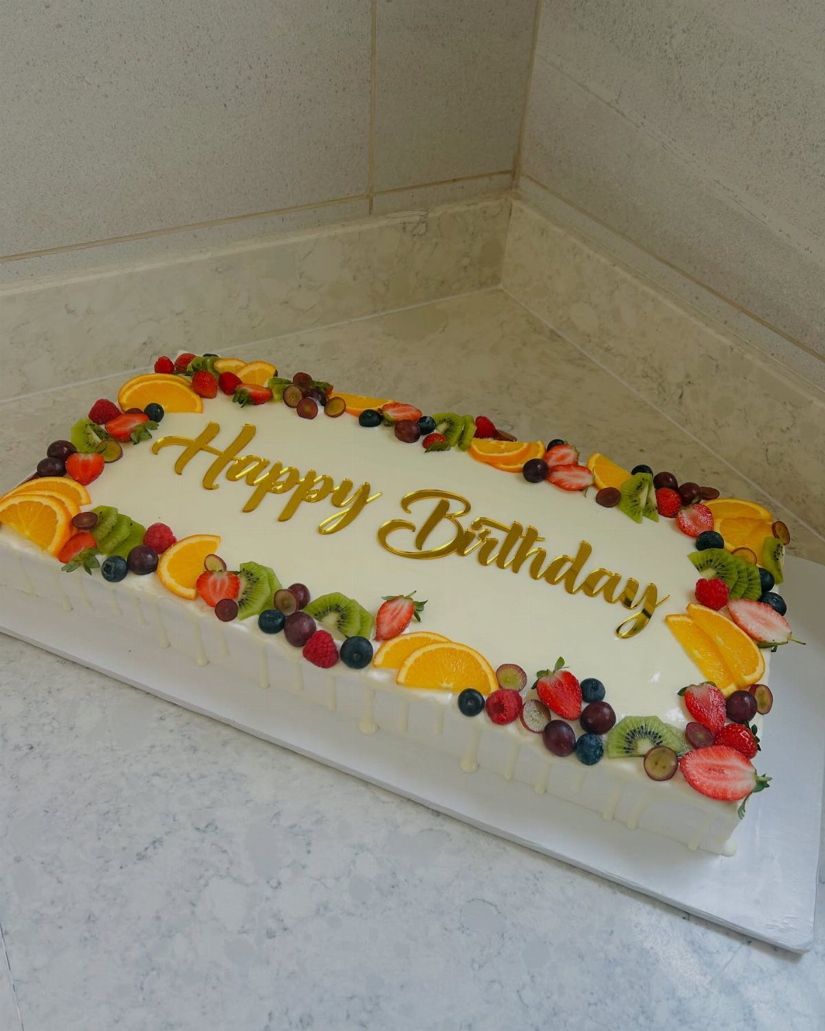 Rectangular white birthday cake topped with fresh sliced strawberries, kiwi, blueberries, and oranges.