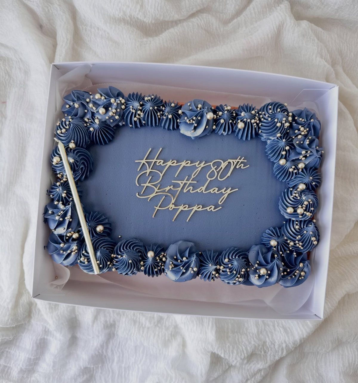 Blue sheet cake with gold 80th birthday lettering and pearl frosting decorations.