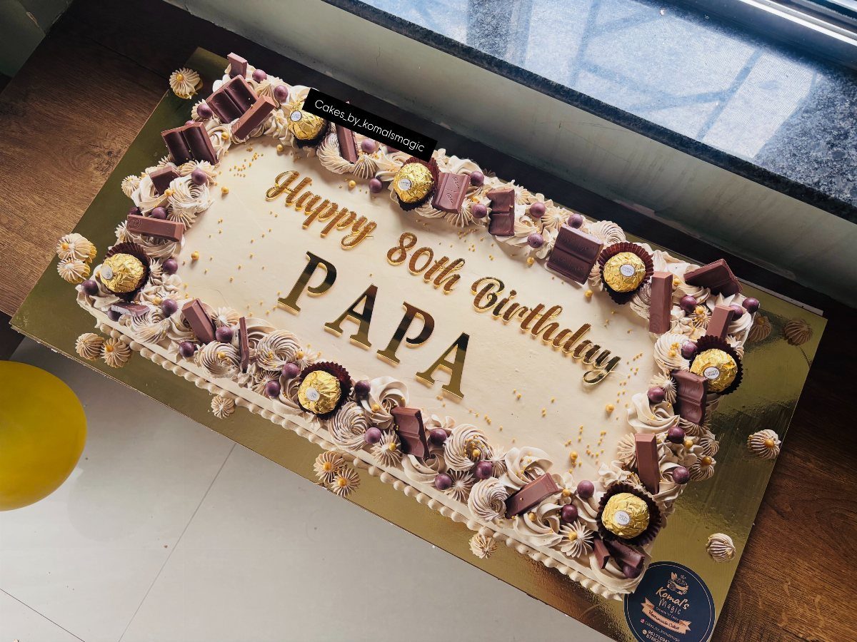 Rectangular white sheet cake decorated with chocolates and gold text for 80th birthday
