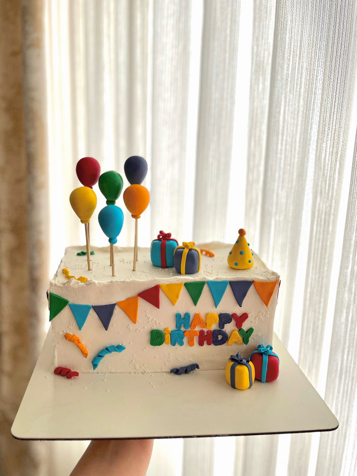 White sheet cake decorated with colorful balloons, bunting, and Happy Birthday lettering.