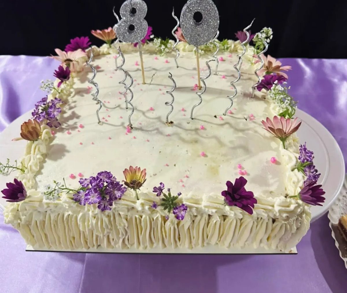 White rectangular sheet cake with purple flowers and silver 80 birthday toppers