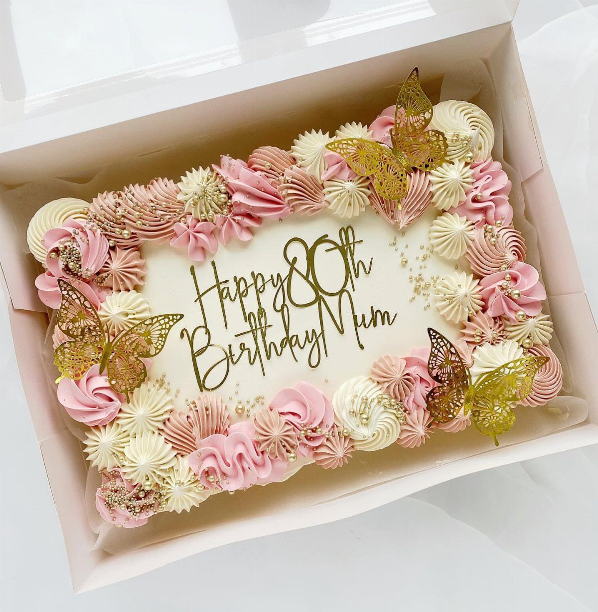 Rectangular sheet cake with pink and white frosting, gold butterflies, and 80th birthday text.