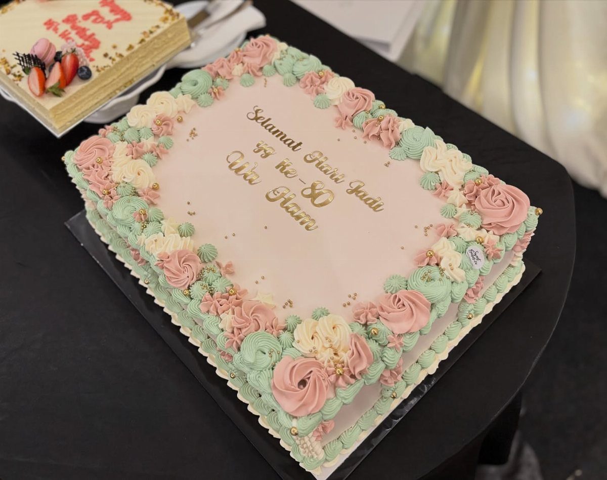 Rectangular pink sheet cake with mint and pink buttercream roses and gold lettering.