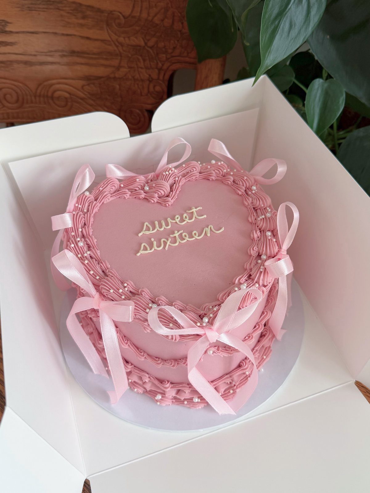 Heart-shaped pink frosted cake with bows and sweet sixteen written on top