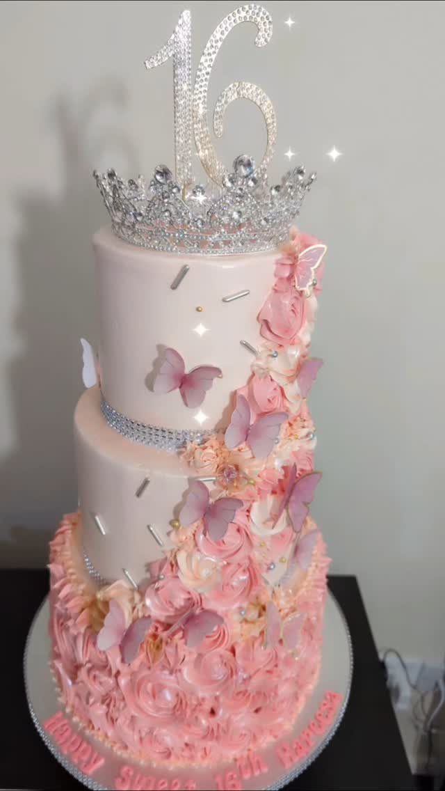 Two-tier pink birthday cake with roses, butterflies, a tiara, and number 16 topper.