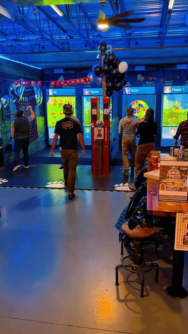 People playing arcade games at a birthday party with balloons and banners.