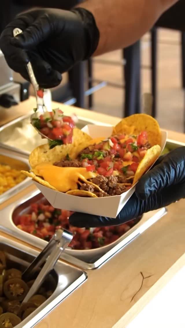 Nachos with cheese and salsa being prepared by hands in black gloves.