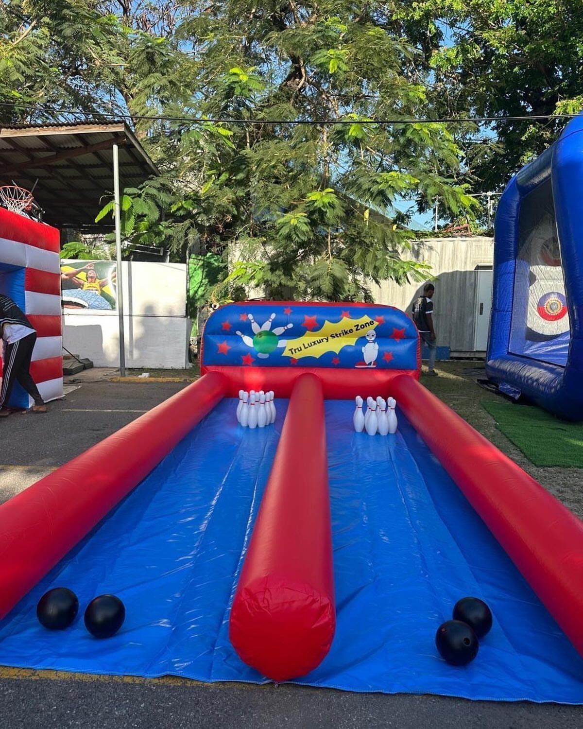 Inflatable bowling game with blue lanes, red dividers, and black bowling balls outdoors.
