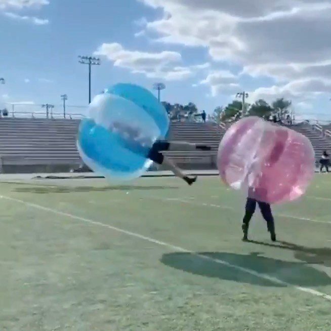 People in blue and pink inflatable bubbles colliding on a green sports field.