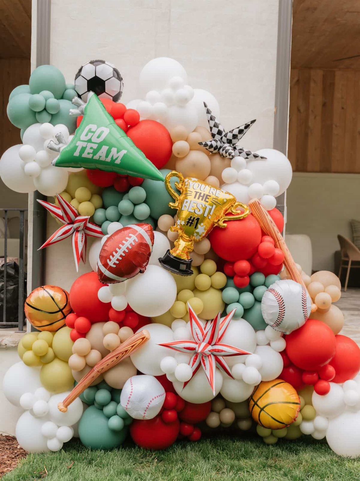 Sports-themed balloon arch with football, basketball, and baseball balloons and a gold trophy.