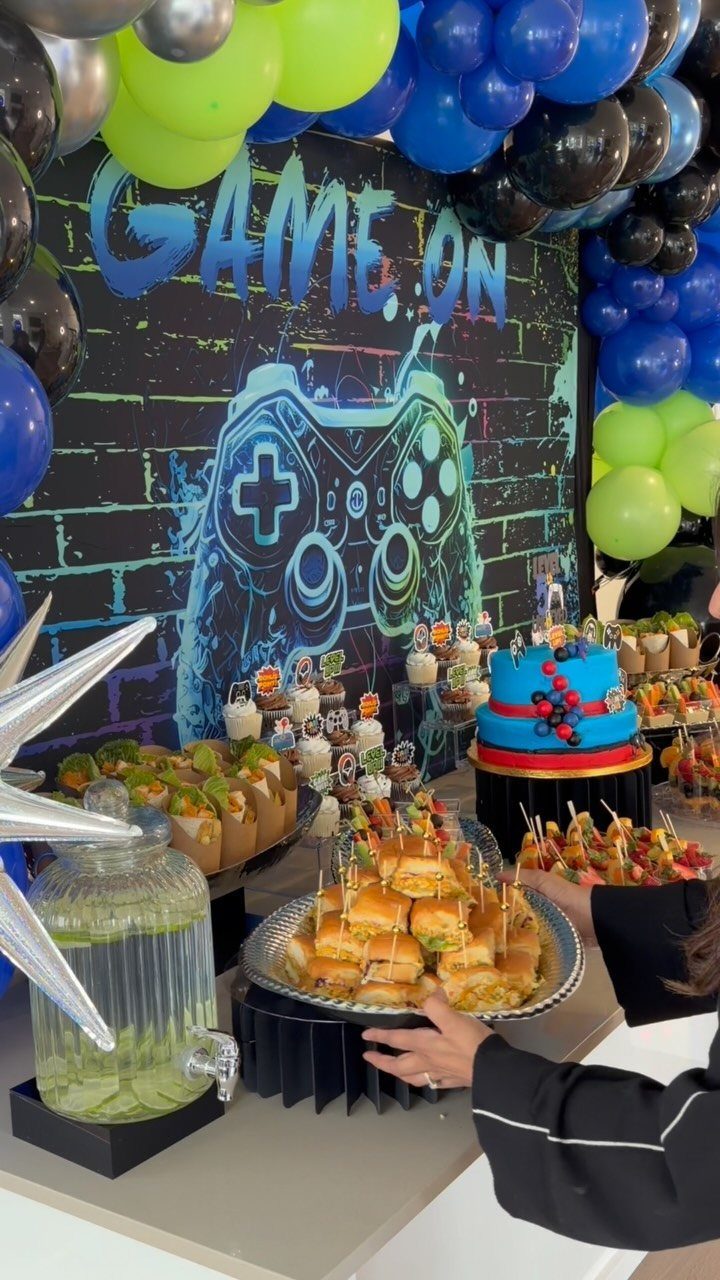 Party food table with a gaming themed backdrop and colorful balloons.
