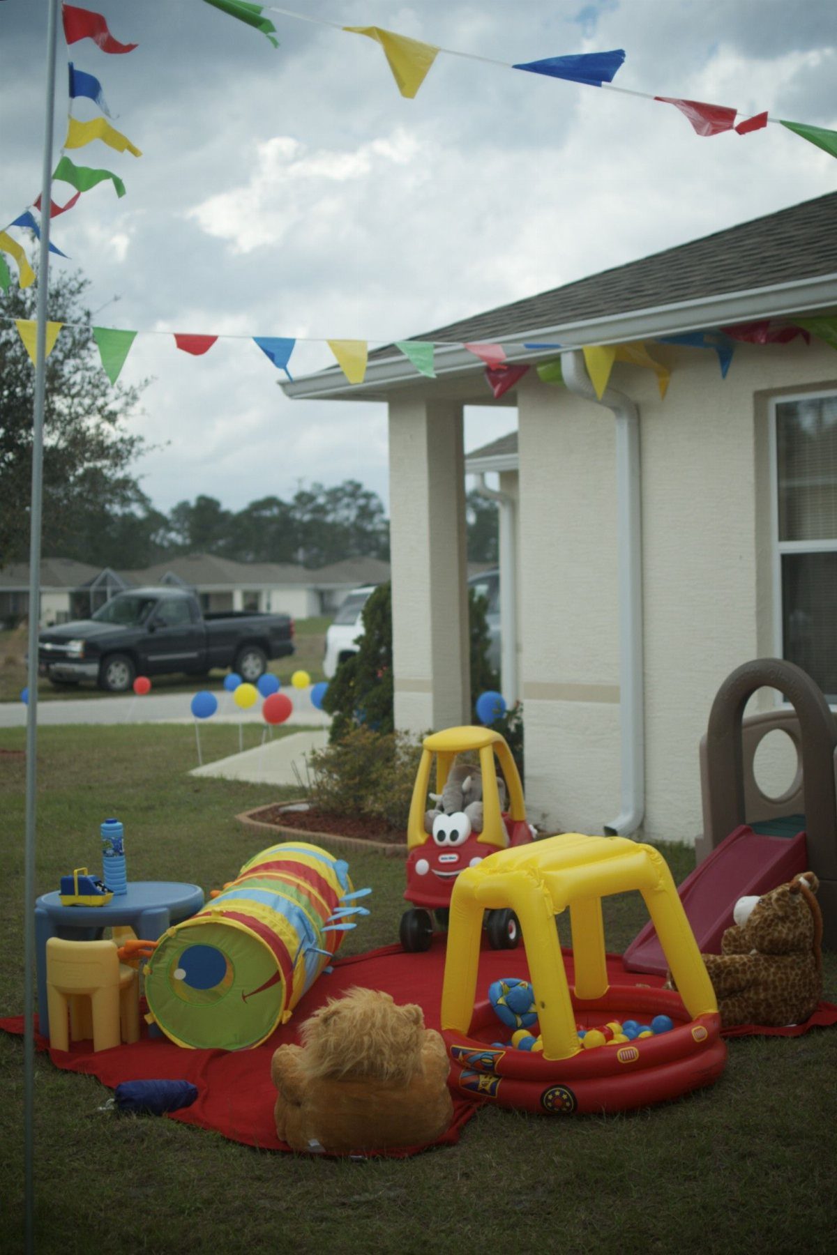 Toddler party setup with colorful toys and bunting flags in a grassy backyard