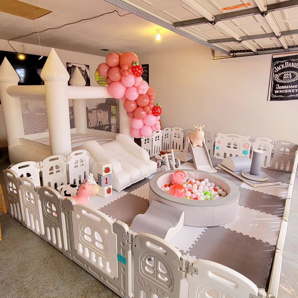 White plastic playpen with ball pit and inflatable bounce house in a garage.