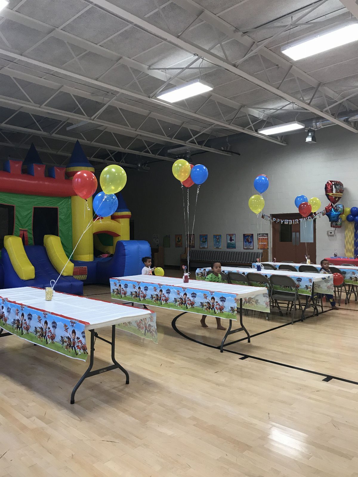Party tables with balloons and a large inflatable bounce house in a gym.