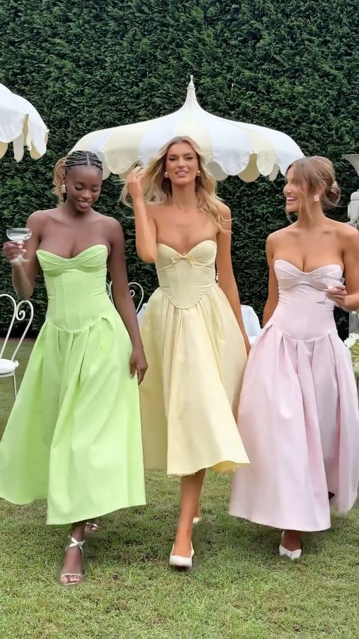 Three women wearing colorful strapless midi dresses walking on grass outdoors