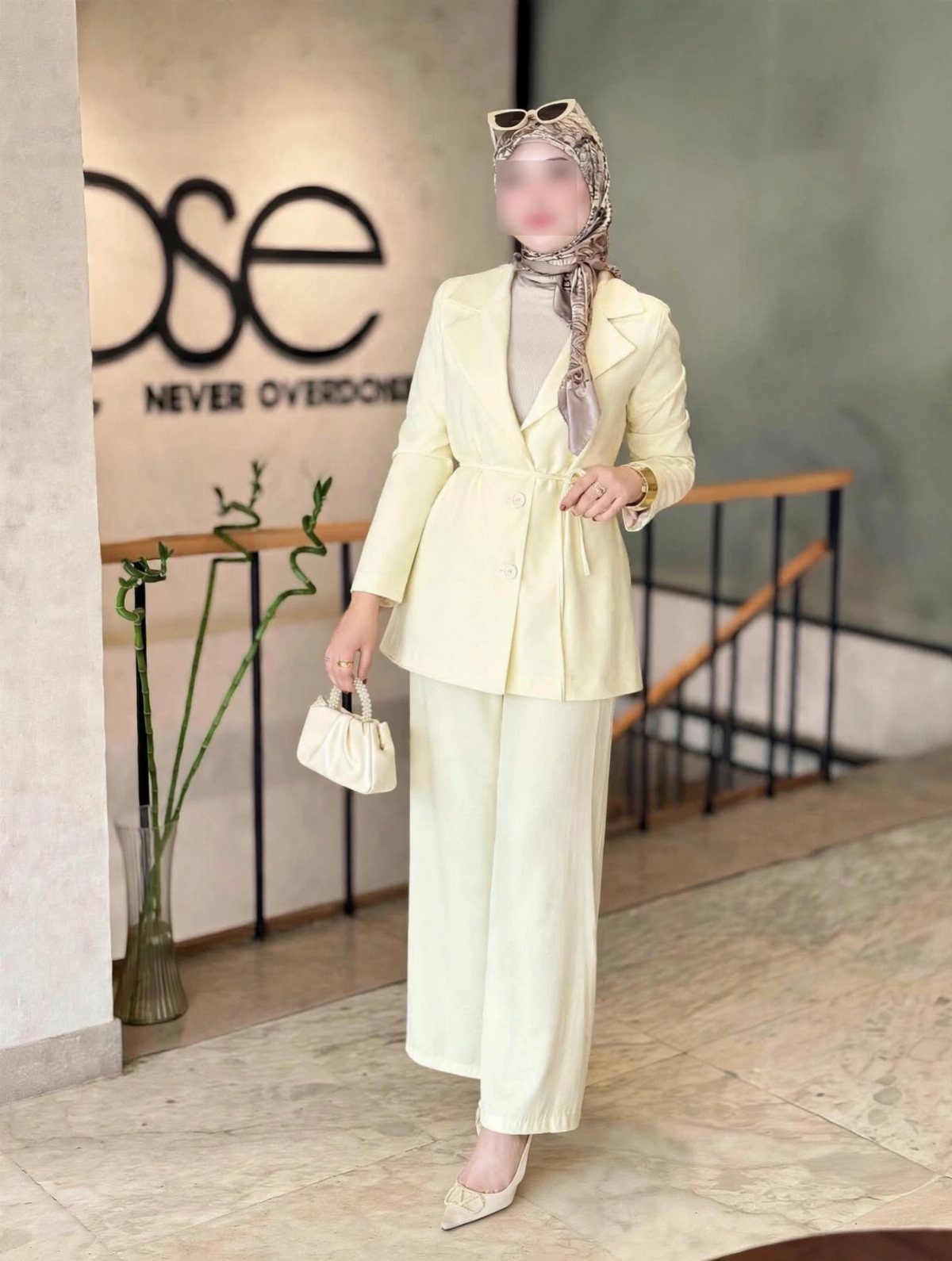 Woman in a pale yellow pastel suit set with a beige hijab and handbag.