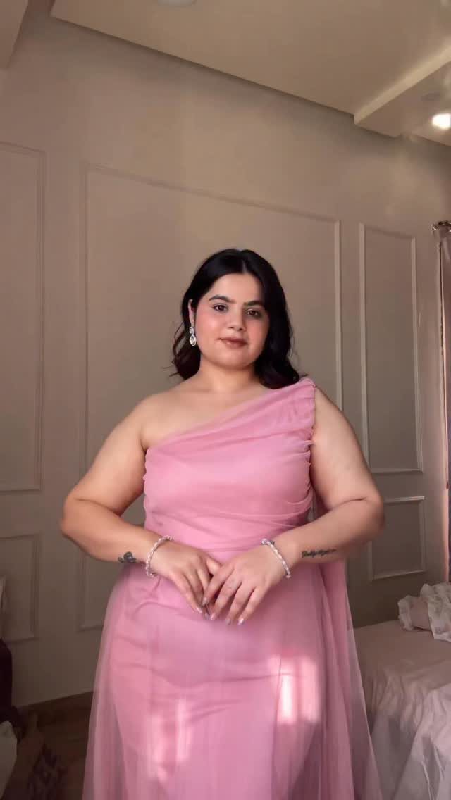 Woman wearing a one-shoulder pink gown standing against a neutral paneled wall